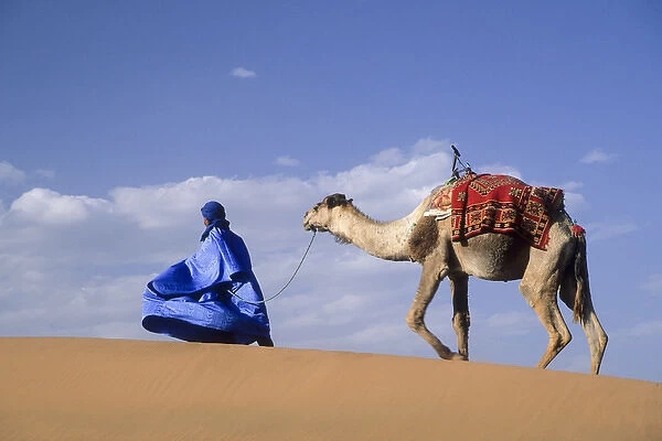 Africa, Morocco, Tinfou (near Zagora) Man in traditional dress leading camel on sand dunes