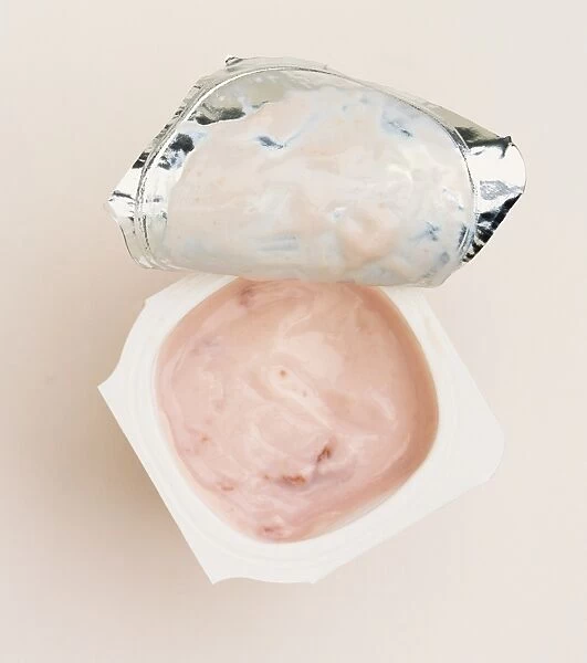 Pot of yogurt, foil lid pulled back to show pink coloured yogurt, above view
