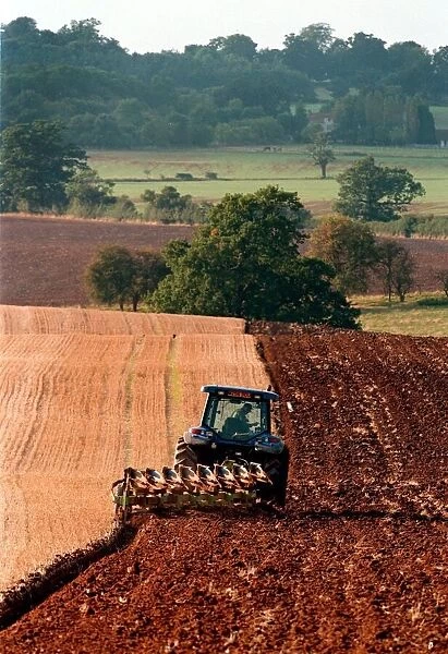 A farm worker steers his tractor and plough in the early evening light on land
