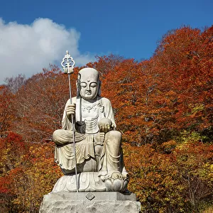 Big shizo statue in front of fire red autumnal leaves at beautiful Japanese temple surrounded by autumn colors, Osorezan Bodaiji Temple, Mutsu, Aomori prefecture, Honshu, Japan, Asia