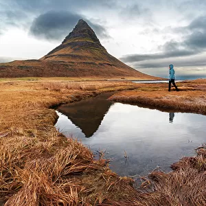Woman walks in front of the famous Kirkjufell mountain reflecting in the water of a small lake, Snaefellsnes Peninsula, Western Iceland, Iceland, Polar Regions
