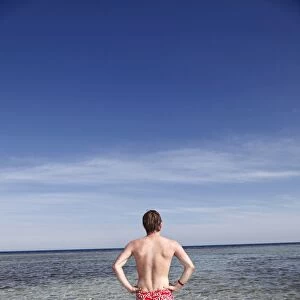 Rear view of a man on summer holiday standing in the sea on the beach