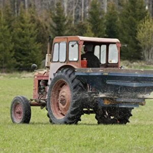 Tractor with fertilizer spreader, spreading nitrogen granular fertilizer on field, Sweden, may