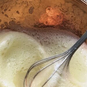 Egg white being beaten in a copper bowl with a balloon whisk