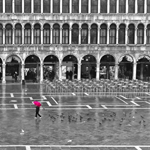One person with a red umbrella crossing the St Marks Square by a rainy day in winter in Venice, Italy