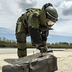 Soldier dressed in bomb suit inpecting a simulated improvised explosive device
