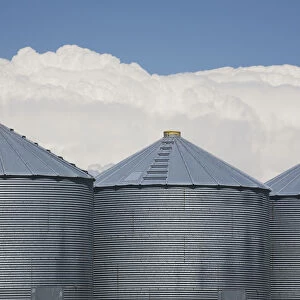 Three Grain Bins With Dramatic Thunder Storm Clouds In The Background And Blue Sky; Alberta, Canada