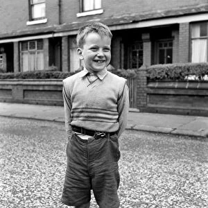 Young boy wearing a sleveless sweater over his shirt and baggy shorts standing in
