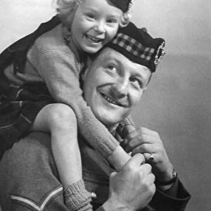 Young girl wearing a hat with tartan design sitting of her fathers shoulder